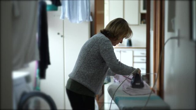 Older woman ironing clothes, candid domestic housewife at laundry room