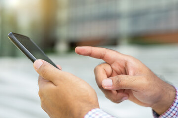 Close up businessman using modern smartphone device typing text message in social media while sitting on stairs outdoor. Happy male spending free time in break of working.