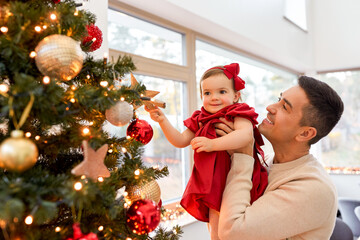 winter holidays and family concept - happy middle-aged father and baby daughter decorating christmas tree with star at home