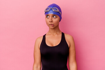 Young swimmer mixed race woman isolated on pink background confused, feels doubtful and unsure.