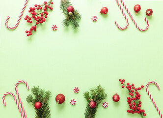 Christmas decoration border on pastel green background. Fresh fir twig, red balls and candy canes