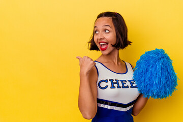 Young cheerleader mixed race woman isolated on yellow background points with thumb finger away,...