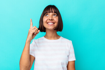 Young mixed race woman isolated on blue background indicates with both fore fingers up showing a...