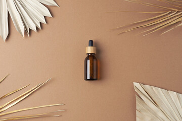 Cosmetic bottle with palm leaf on brown background. Flat lay