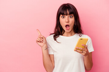 Young caucasian woman holding a mobile phone isolated on pink background pointing to the side
