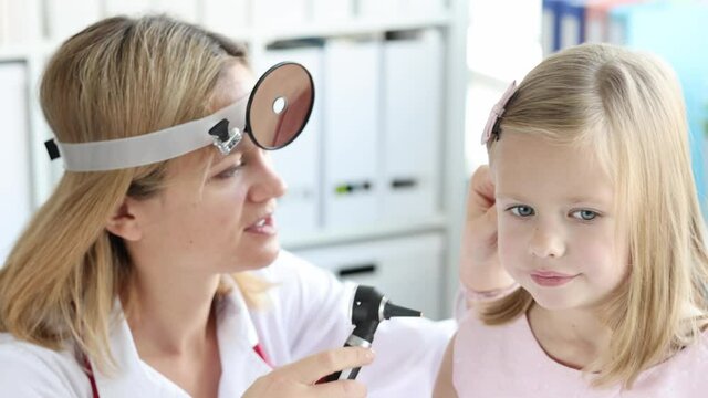 ENT woman looks at ear of little girl with otoscope slow motion 4k movie
