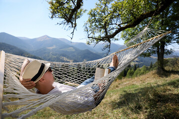 Young man reading book in hammock outdoors on sunny day