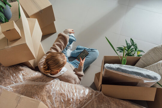 Woman using mobile phone on floor with cardboard boxes around at new home