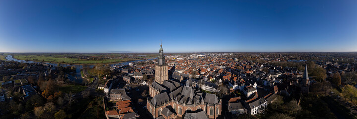 Fototapeta na wymiar Tower town Zutphen in The Netherlands with medieval Hanseatic city center on the river IJssel and Walburgiskerk centrally in the frame. Aerial panorama of Dutch settlement against a clear blue sky.