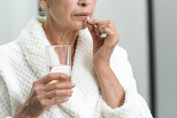 Elderly woman taking pills and holding glass of water