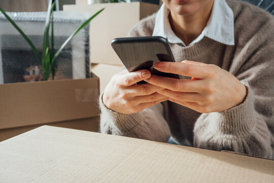 Woman text messaging at cardboard box in new home
