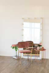 Soft home decor in a gentle tonality, a pink jug, a candle, a vase with pink beautiful flowers on a white wall background and in a round pink table a tray. Interior.