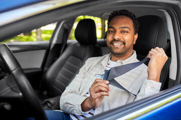 transport, safety and people concept - happy smiling indian man or driver fastening seat belt in car