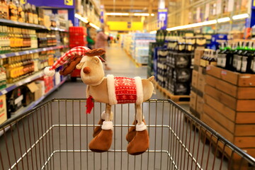 Funny Christmas deer on supermarket trolley. Shopping in the shop before the New Year, sale. A basket in wholesale store, background of blurred shelves with groceries and goods.