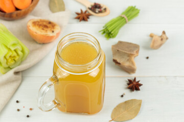 Bone beef broth with vegetables and spices. In a tall glass mug. Close-up on a light wooden background