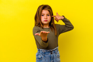 Little caucasian girl isolated on yellow background holding and showing a product on hand.
