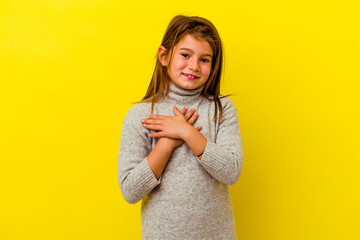 Little caucasian girl isolated on yellow background laughing keeping hands on heart, concept of...