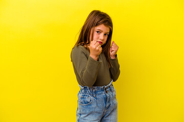 Little caucasian girl isolated on yellow background throwing a punch, anger, fighting due to an...