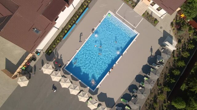 Aerial view of people relaxing in the swimming pool with blue water at small luxury hotel, camera rotates and fly up