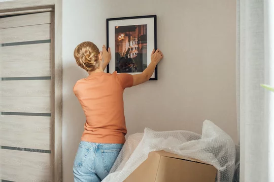 Woman mounting picture frame on wall in new apartment