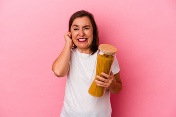 Middle age caucasian woman holding a pasta jar isolated on pink background covering ears with hands.