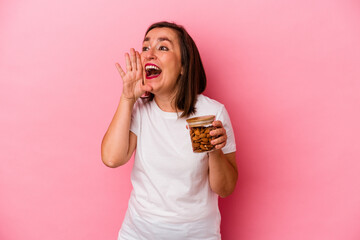 Middle age caucasian woman holding an almond jar isolated on pink background shouting and holding palm near opened mouth.