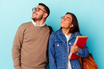 Young mixed race student couple isolated on blue background dreaming of achieving goals and purposes