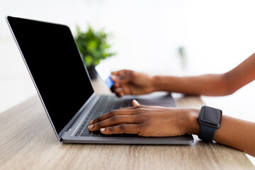 Naklejka premium Closeup of black lady using laptop and credit card to shop online from home, mockup for shopping website on screen