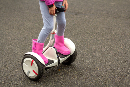 Close-up Of Child Girl Legs In Bright Pink Rubber Boots Riding Segway On Sunny Asphalt Street Copy Space Background.  Kyiv, Ukraine - September 13, 2020