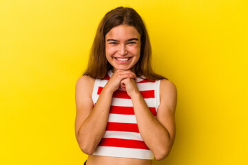 Young caucasian woman isolated on yellow background keeps hands under chin, is looking happily aside.