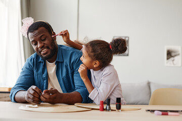 Portrait of African-American single father playing with daughter at home and doing makeup, copy...