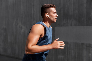 fitness, sport, training and lifestyle concept - young man in earphones running outdoors
