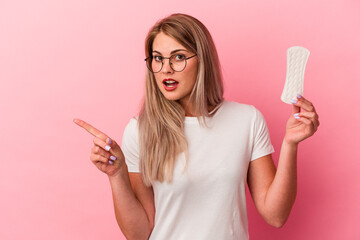 Young russian woman holding a compress isolated on pink background pointing to the side