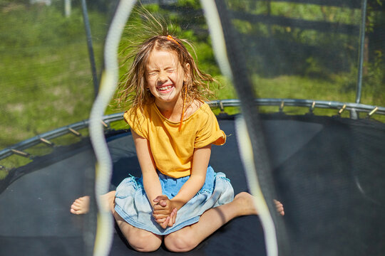 Portrait of  young girl with electrified hair on trampoline outdoors, in the backyard of the house on a sunny summer day, summertime vacation, Happy little child  jumping on trampoline