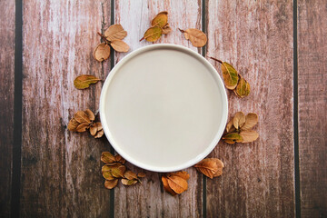 Fototapeta na wymiar Decorative ceramic beige plate and yellow leaves