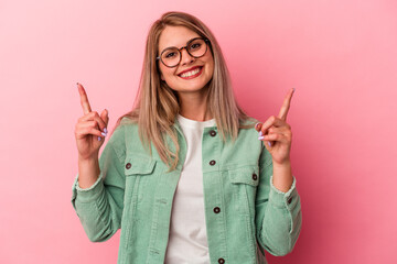 Young russian woman isolated on pink background indicates with both fore fingers up showing a blank...