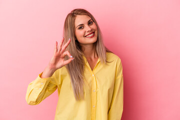 Fototapeta premium Young russian woman isolated on pink background winks an eye and holds an okay gesture with hand.