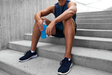 fitness, sport and people concept - tired young man with bottle of isotonic energy drink sitting on...
