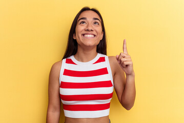Young mixed race woman isolated on yellow background indicates with both fore fingers up showing a...