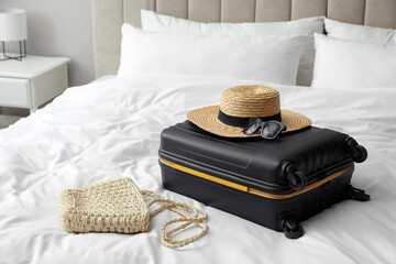 Suitcase packed for trip and summer accessories on bed indoors
