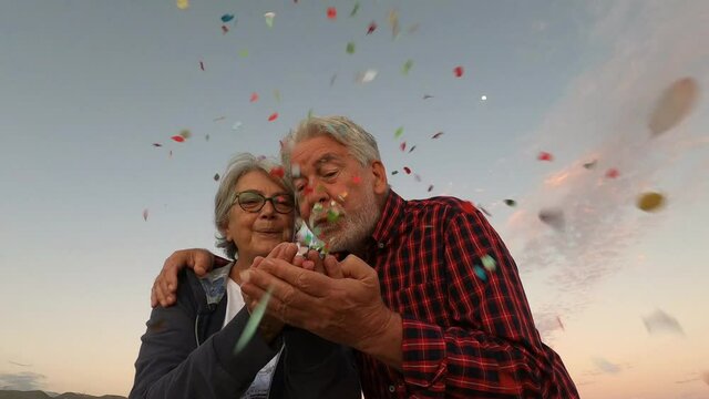 Happy senior couple blowing confetti from their hands