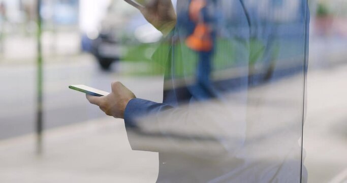 Businessman holding cup of coffee and smartphone at bus stop