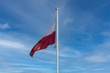 The national flag of Poland flies against a blue sky and a few white clouds.