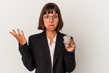 Young mixed race business woman holding a light bulb isolated on white background shrugs shoulders...