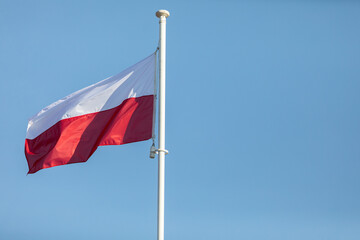 Fototapeta na wymiar The flag of Poland flying in the wind on a tall pole against a blue sky.