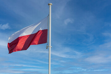 The national flag of Poland flies against a blue sky and a few white clouds.