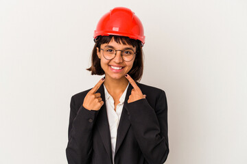Young architect woman with red helmet isolated on white background smiles, pointing fingers at mouth.
