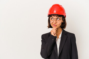 Young architect woman with red helmet isolated on white background looking sideways with doubtful and skeptical expression.