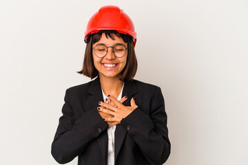 Young architect woman with red helmet isolated on white background laughing keeping hands on heart, concept of happiness.