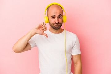 Young caucasian bald man listening to music isolated on pink background  showing a dislike gesture,...